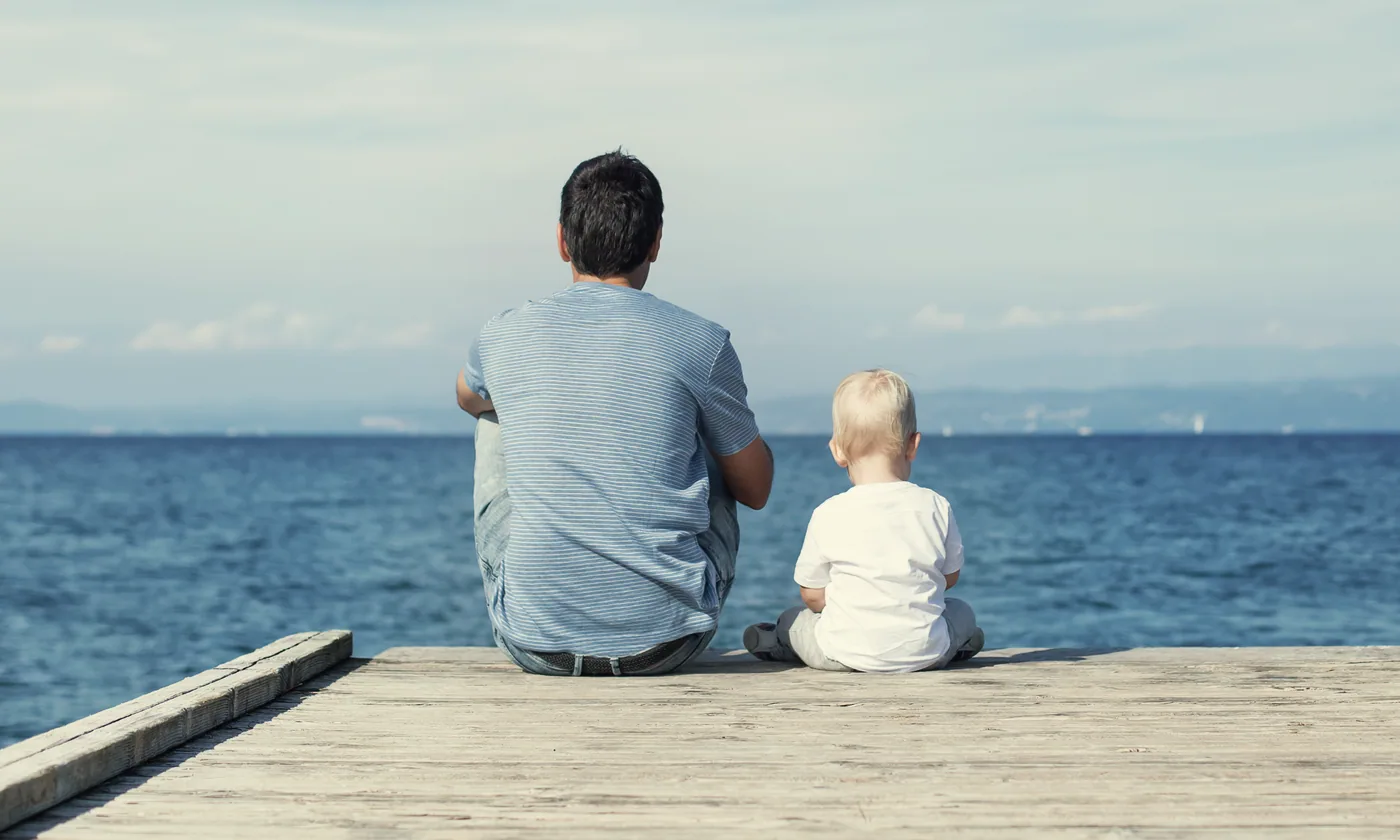 Pai e filho sentados num cais diante do mar